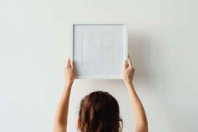 A person holding a white picture frame above their head and placing it on a wall